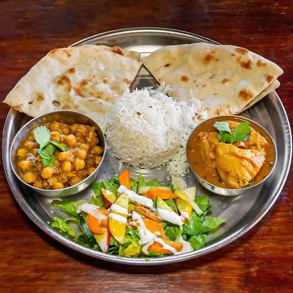 Indian thali with naan, rice, chickpea curry, chicken curry, and a fresh salad.