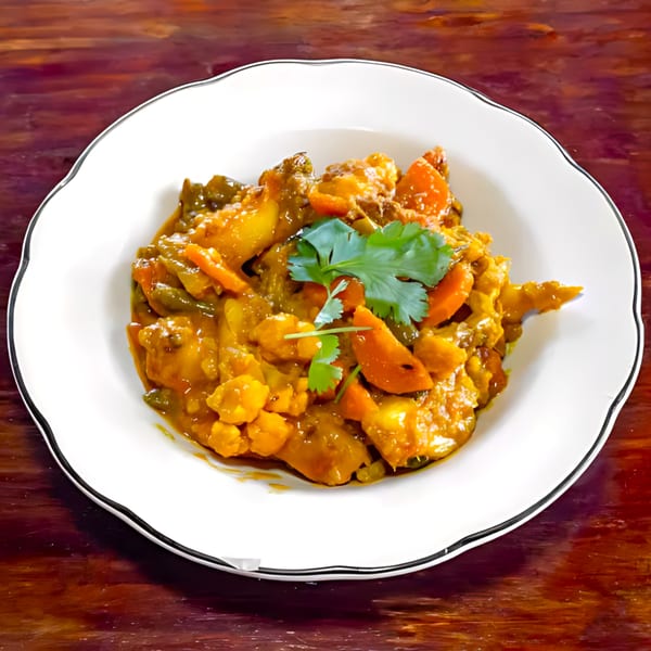 A white plate filled with Indian vegetable curry, garnished with fresh cilantro, on a wooden table.