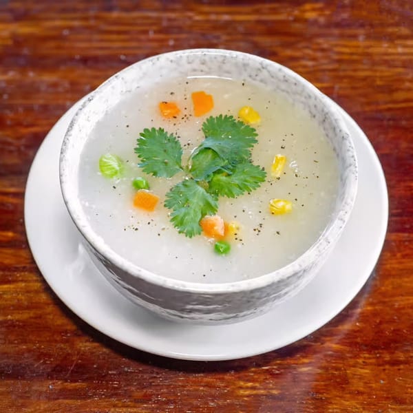 A white bowl of Indian soup with carrots, peas, corn, and cilantro on a wooden table.