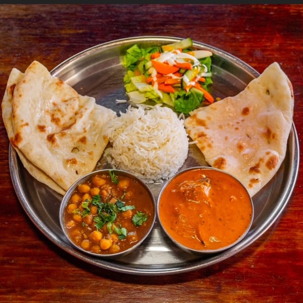 Indian thali with naan, rice, chickpea curry, butter chicken, and a fresh salad.