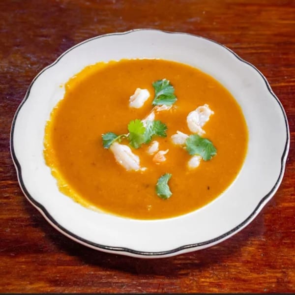 A bowl of orange Indian soup with white crab meat and green cilantro on a wooden table.