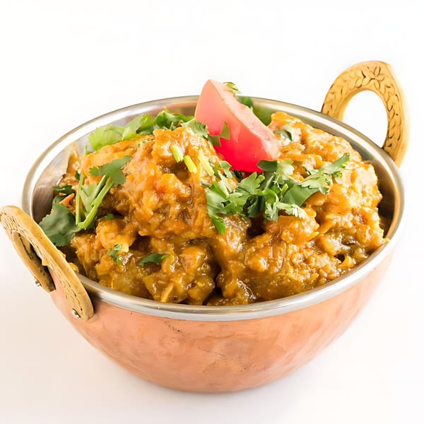 Indian curry in a copper karahi, garnished with fresh cilantro and a tomato slice.