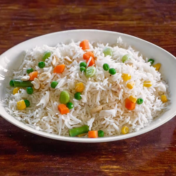 A white oval plate filled with Mount Everest Restaurant's vegetable pilau rice, featuring peas, carrots, and cashews.