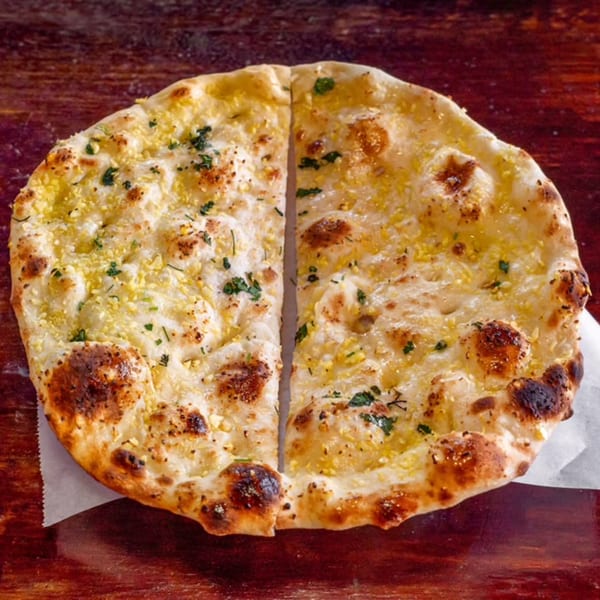 Two pieces of golden-brown garlic naan bread, sprinkled with herbs, on a wooden surface.
